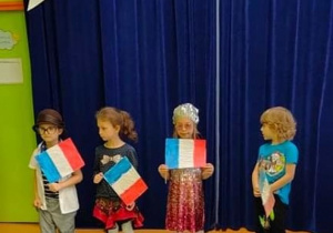Sala gimnastyczna. Francuzki pokaz mody. Czworo dzieci trzyma w ręku francuską flagę i prezentuje swoje stroje przygotowane na pokaz mody.